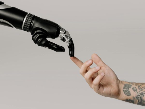 A robotic hand and a human hand reach toward each other, with their fingers nearly touching, against a plain background.