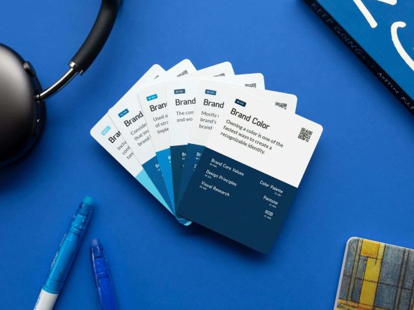 A fanned stack of brand color reference cards on a blue surface, next to headphones, a blue pen, and part of a notebook.