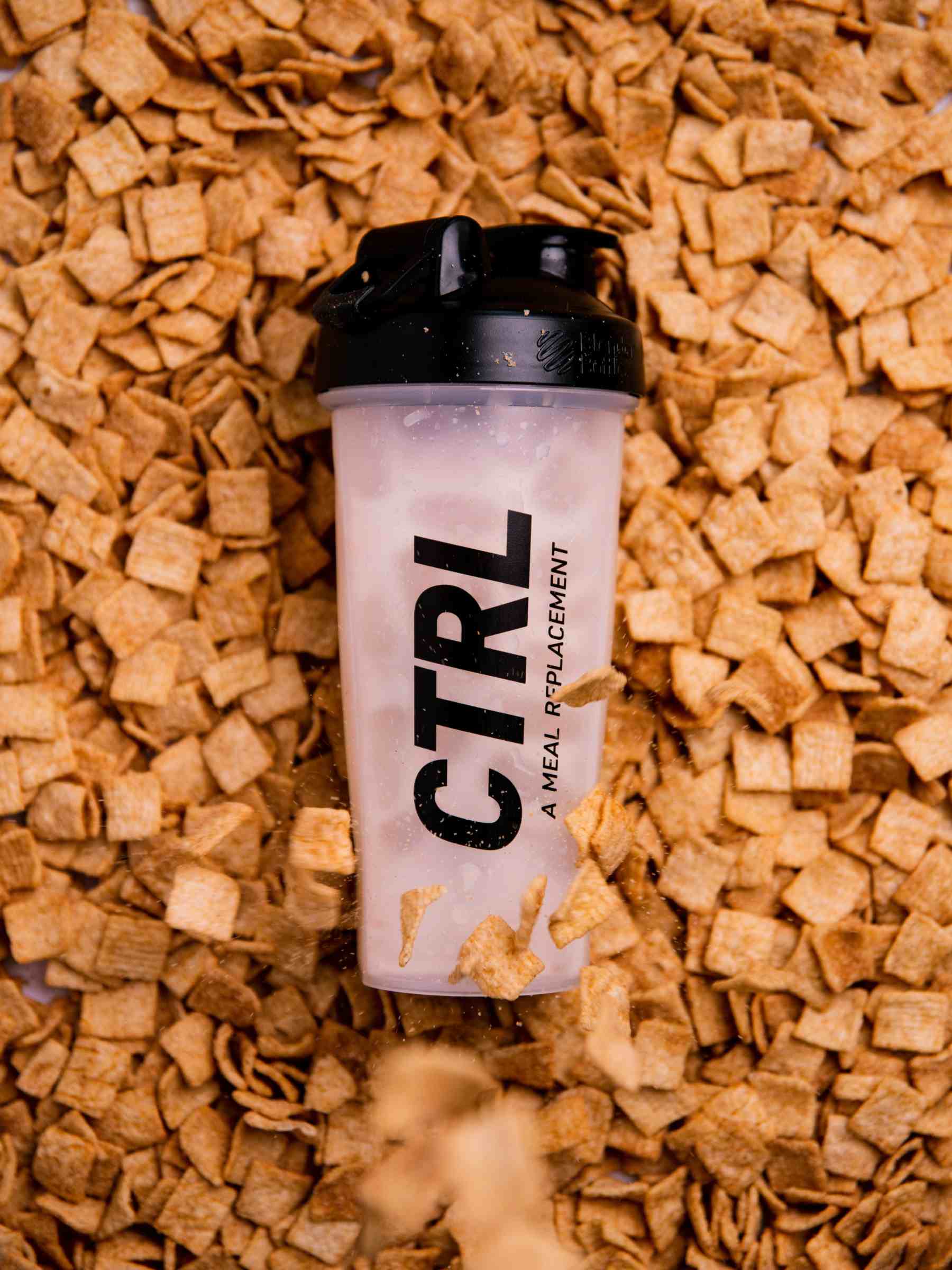 A plastic shaker bottle labeled “CTRL: A Meal Replacement” lies on a pile of square-shaped cereal pieces.